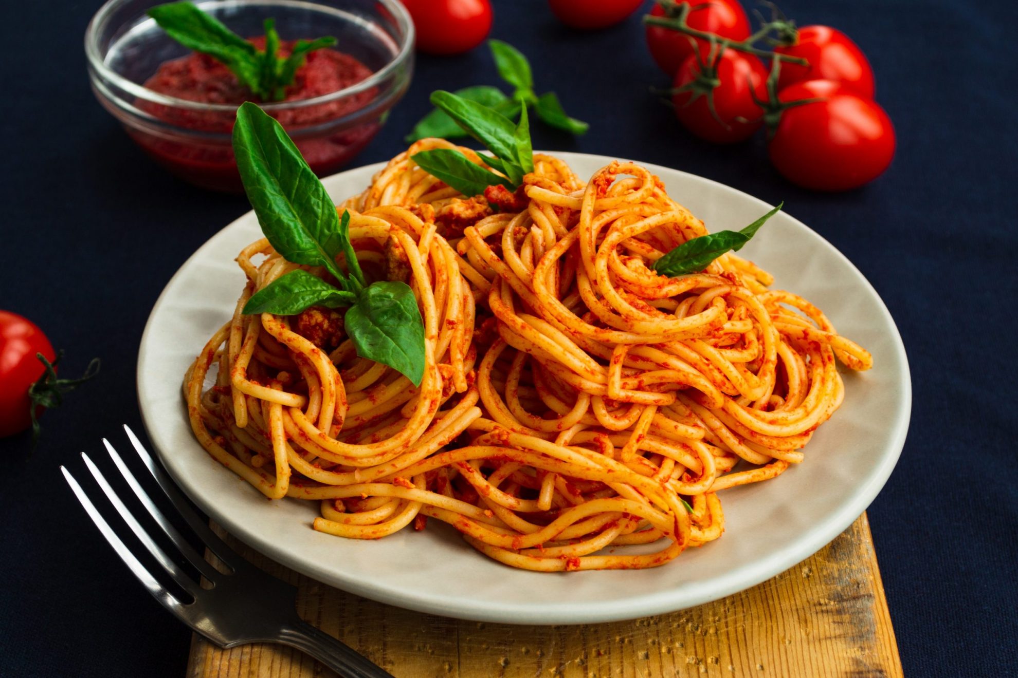 Photo of plate of spaghetti with fork and tomatoes beside it illustrates blog: "Where Does Spaghetti Come From?"