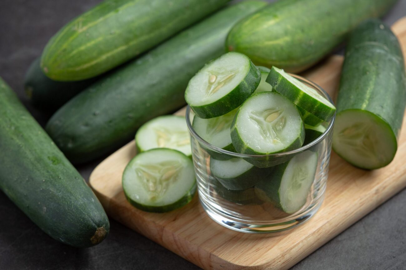 Closeup of sliced cucumbers in a glass atop a cutting board illustrates blog "Are Cucumbers Berries?"