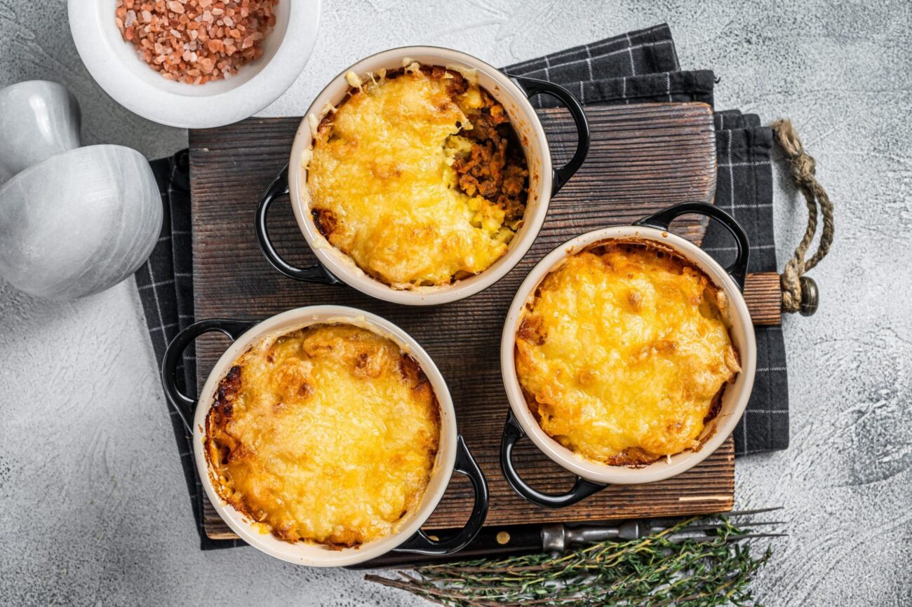 Three shepherd's pies placed atop a wooden board illustrate blog: "Can You Freeze Shepherd's Pie Before Baking It?"