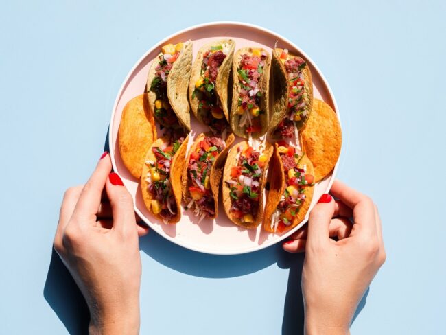 OLYMPUS DIGITAL CAMERA Closeup of person holding plate with tacos illustrates blog "5 Taco Ideas You Need To Try"