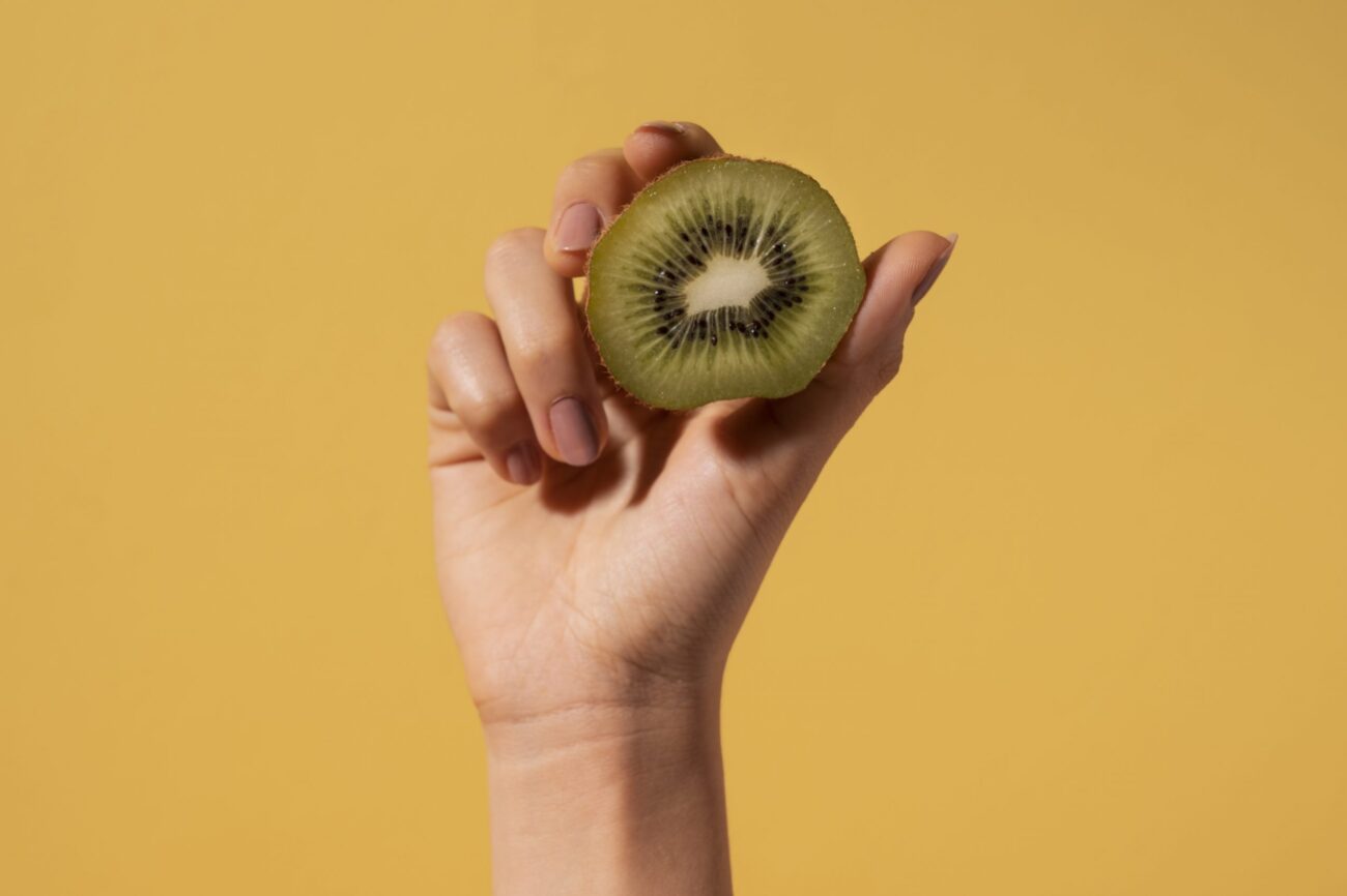 kiwi-fp Closeup of woman holding kiwi cut in half illustrates blog "Will Kiwis Ripen After Being Picked?"
