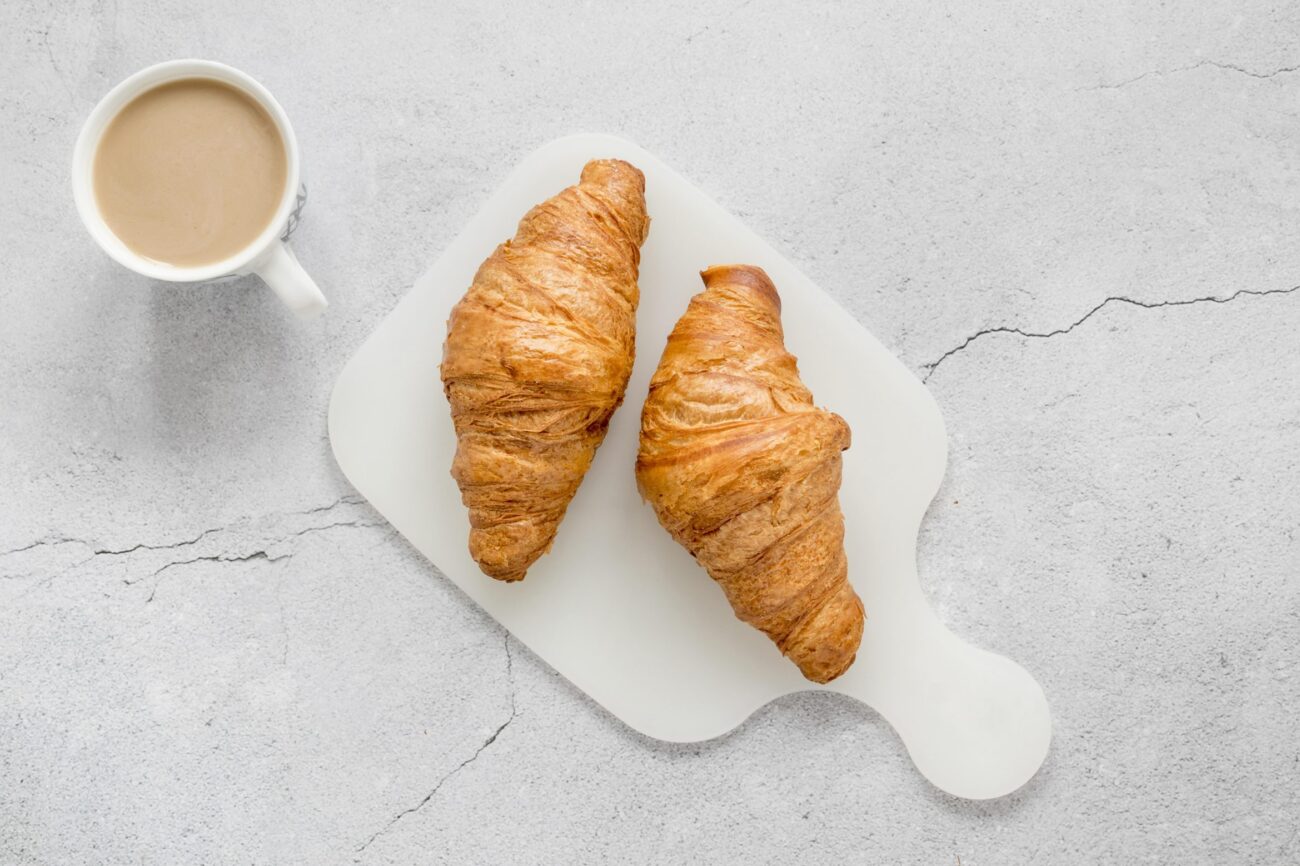 croissants-fp Photo of two croissants with cup of coffee with milk illustrate blog "Are Croissants Made With Eggs?"