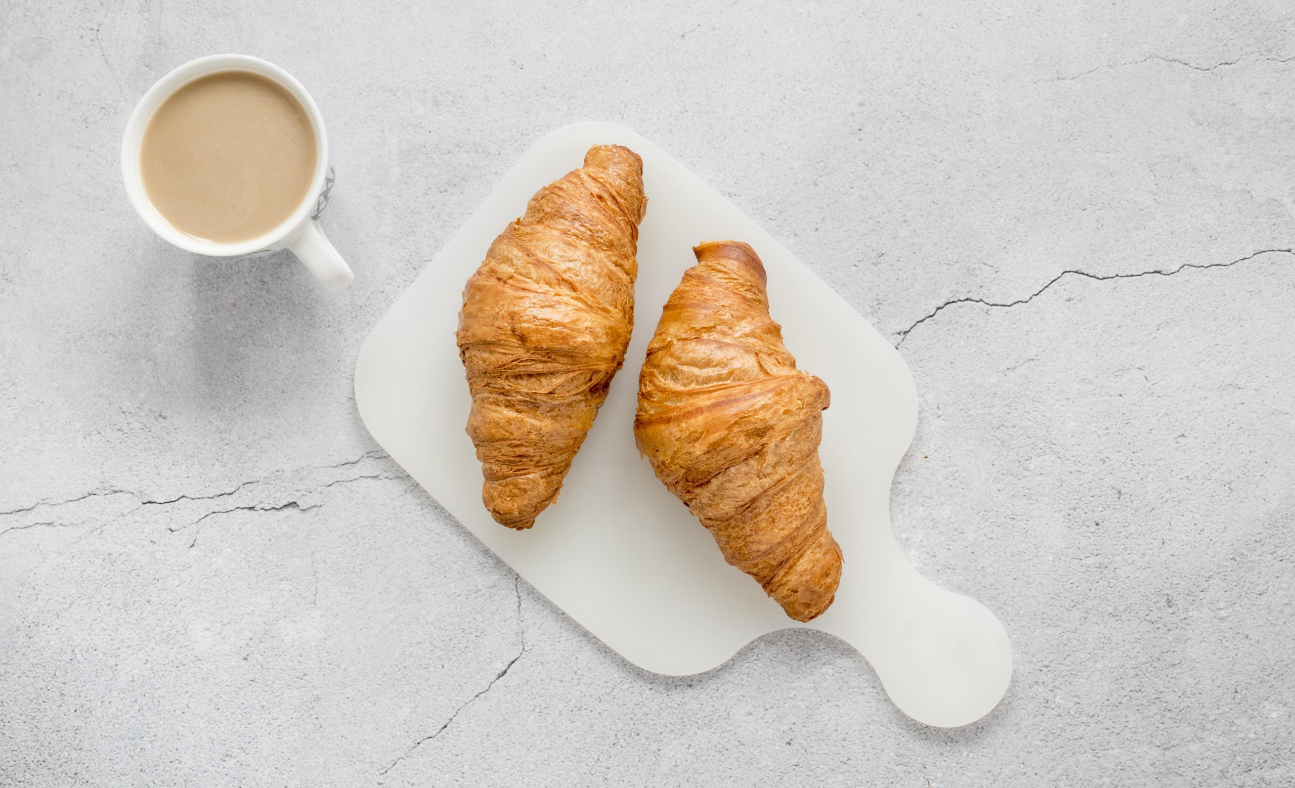 Photo of two croissants with cup of coffee with milk illustrate blog "Are Croissants Made With Eggs?"
