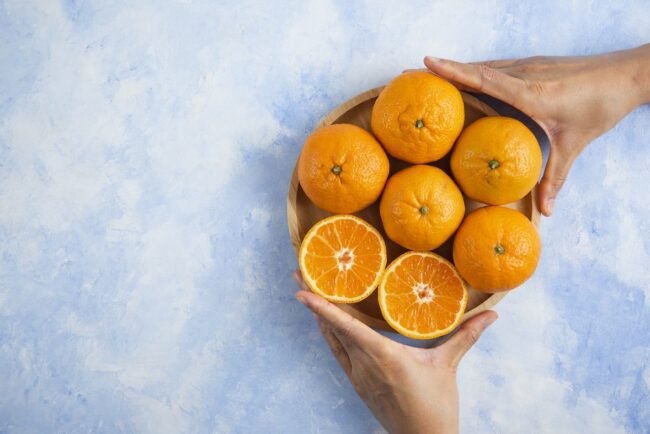 Female hand taking slice from pile. Clementine mandarins on blue background Closeup of oranges.