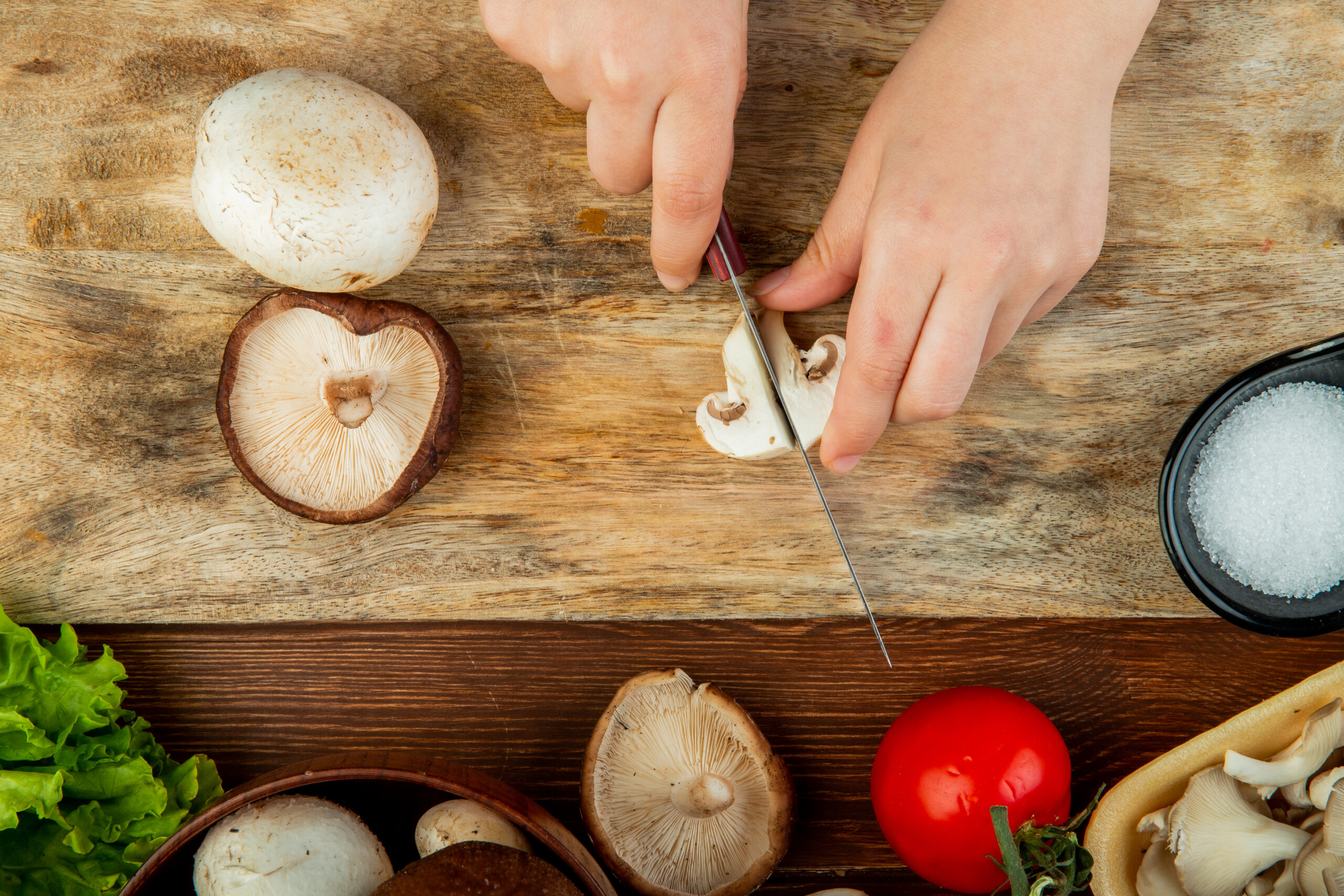 top-view-female-hands-cutting-fresh-mushrooms-wooden-cutting-board-fresh-tomatoes-wooden-rustic-table-scaled