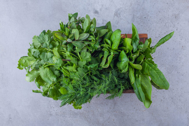 Wooden box of healthy fresh greens on blue background