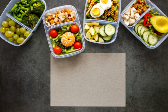 office team eating healthy meal prep containers at modern workspace table with fresh food, salads and balanced meals, natural lighting, realistic professional setting